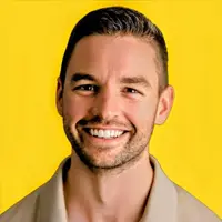 Smiling man with short hair and stubble against a bright yellow background.